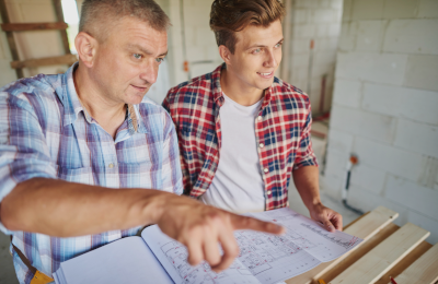 source-de-chaleur-installateur-diagnostic-chauffage-bois deux-hommes-chemises-a-carreaux-sur-chantier-maison-tenant-plan
