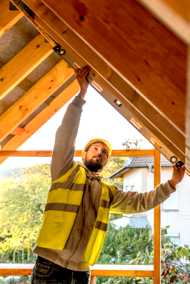 source-de-chaleur-installateur-toit-chauffage-bois artisan-avec-niveau-sous-les-toits-portant-casque-securite-gilet-jaune